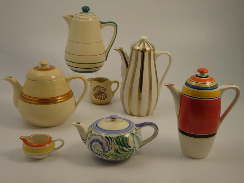 The coffee pot on the extreme right, with banded pattern 7670, is a shape which Susie Cooper regarded as being hers. It was made by Kirklands for Gray's Pottery and was in use until well after Susie Cooper had left the company. The other shapes in the picture may well have resulted from its general design theme in subsequent years: Soup jug - made by Kirklands for Grays - mark R2. Teapot - sourced from Johnson Brothers - pattern A2467, mark N2. Creamer - made by Kirklands for Grays - pattern A4169 Woodgrave, mark R2. Coffee pot - sourced from Johnson Brothers - pattern A961, mark N2. Creamer - maker unknown - pattern 9104, part-mark N2. Teapot - possibly made by Kirklands for Grays - pattern A2288, mark N2.